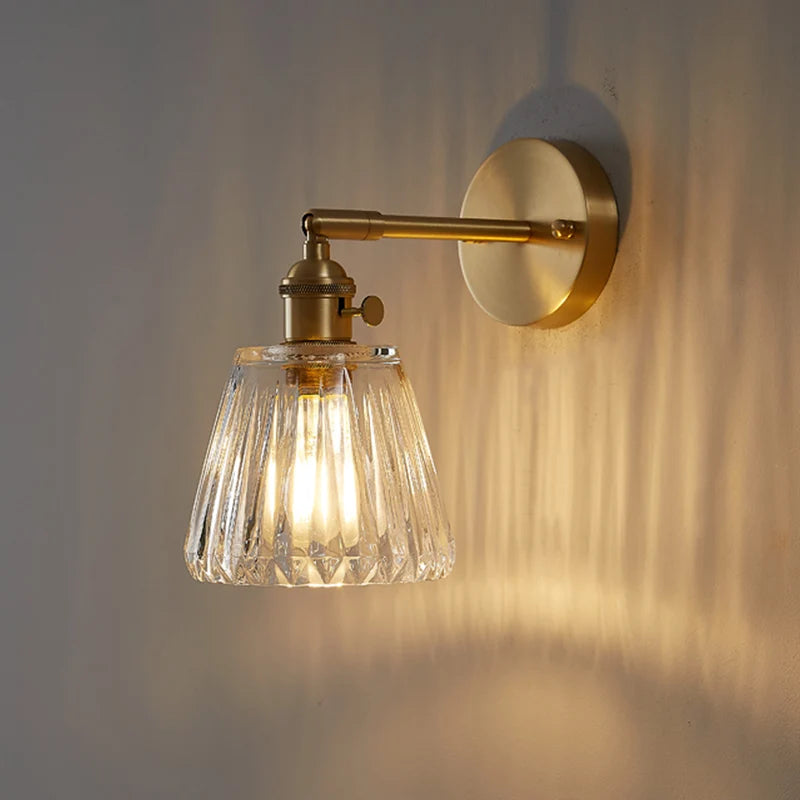 Wall-mounted light fixture with glass shade and gold finish on a neutral wall.